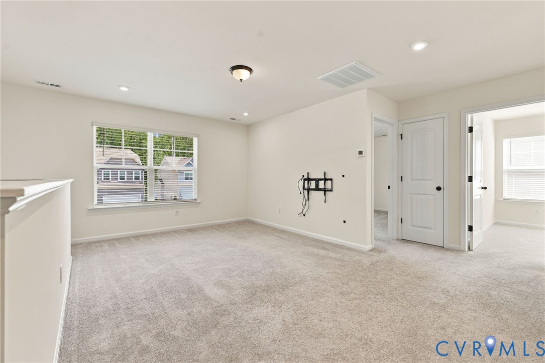 Neutral-toned carpeting, recessed ceiling lighting, a flush-mount light fixture, and white interior doors with dark hardware
