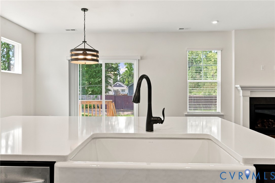 Kitchen island featuring a white countertop, farmhouse-style sink, matte black gooseneck faucet, drum-style pendant light, and sliding glass door access
