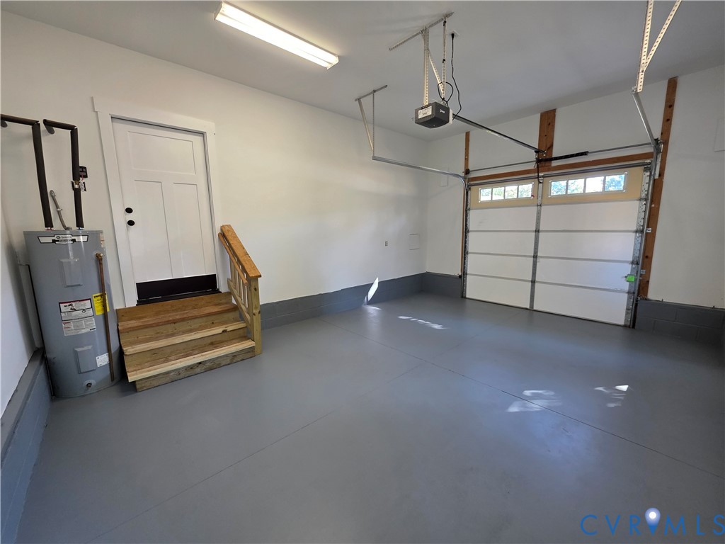 Attached two-car garage featuring a grey epoxy-coated floor, automatic sectional door with glass inserts, white paneled entry door, and wood-finish stair treads with railing