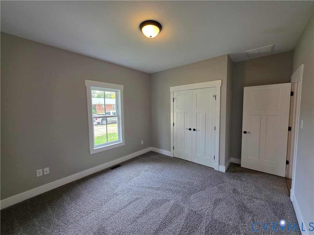 Room featuring neutral-toned walls, carpeting, a single-pane window with white trim, a double-door closet with shaker-style panels, and a flush-mount ceiling light fixture