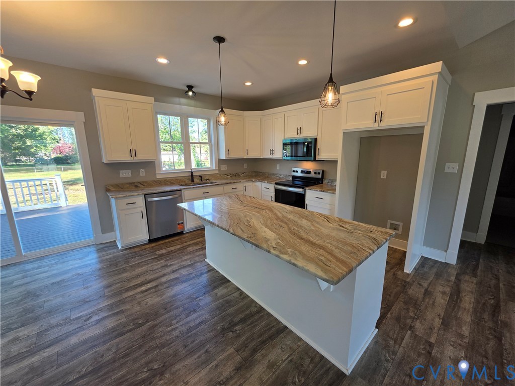 Kitchen featuring white shaker-style cabinetry, natural stone countertops, a central island with an extended breakfast bar, wood-finish flooring, and pendant lighting