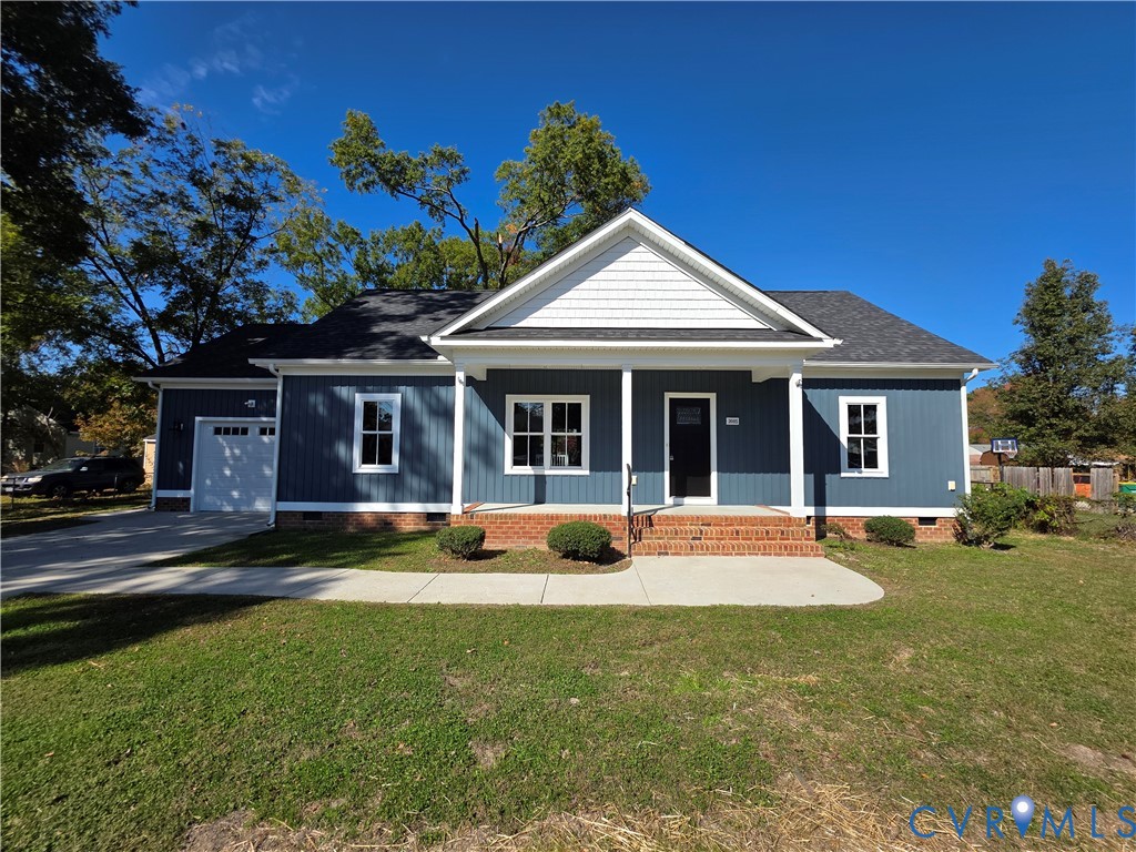 Blue vertical siding exterior featuring a covered front porch, brick foundation detailing, attached garage, and a concrete walkway