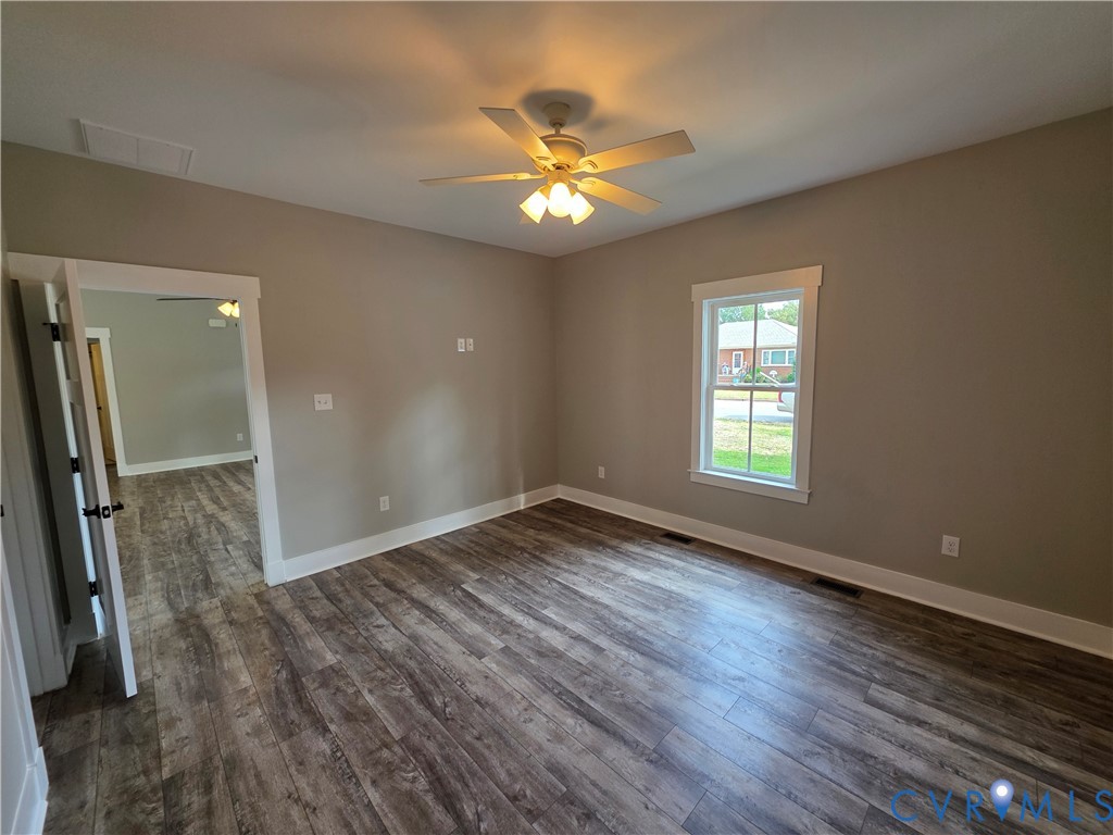 Neutral-toned room featuring wood-finish flooring, a multi-blade ceiling fan with integrated lighting, and a window with white trim