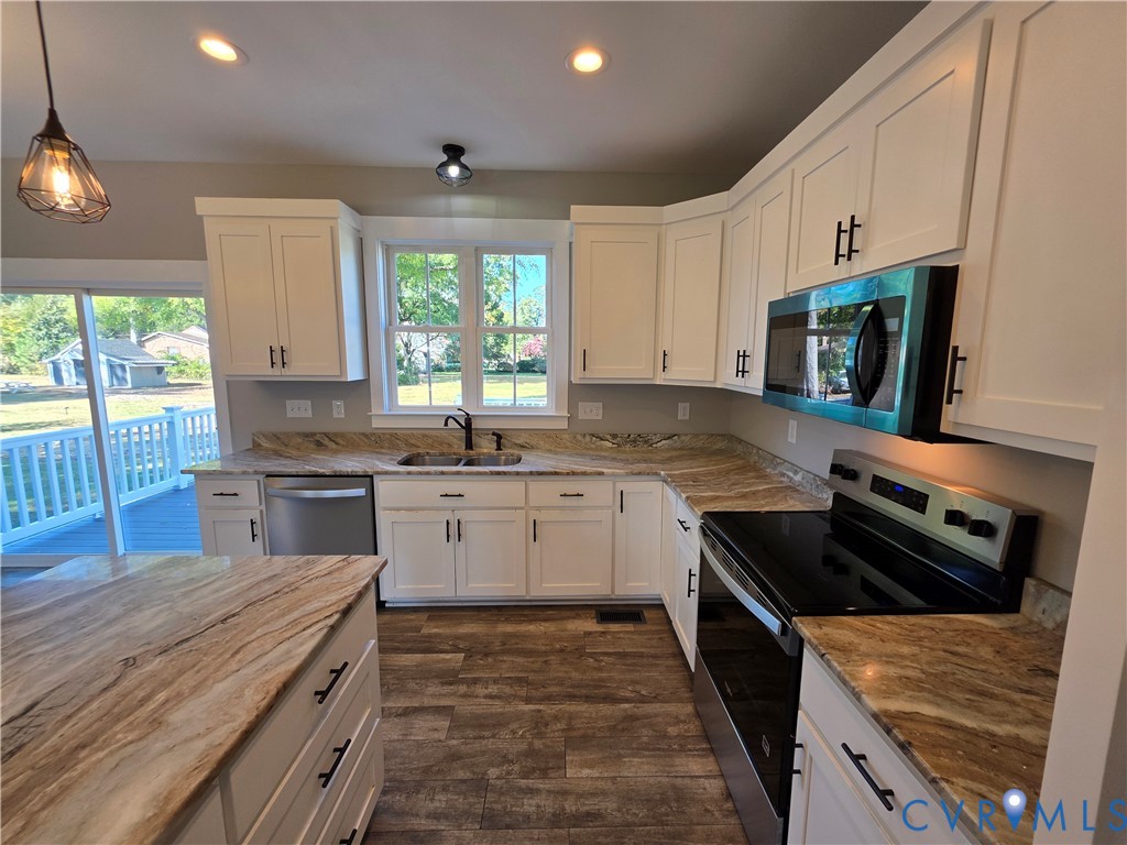 Kitchen featuring white cabinetry with dark hardware, stone-finish countertops, stainless steel appliances, and wood-finish flooring