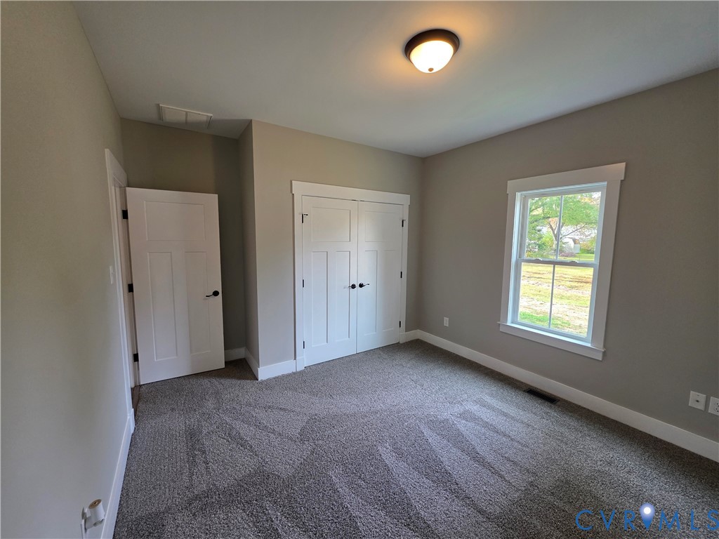 Interior room featuring neutral wall tones, double-door closet cabinetry, a multi-pane window with white trim, and plush carpeting