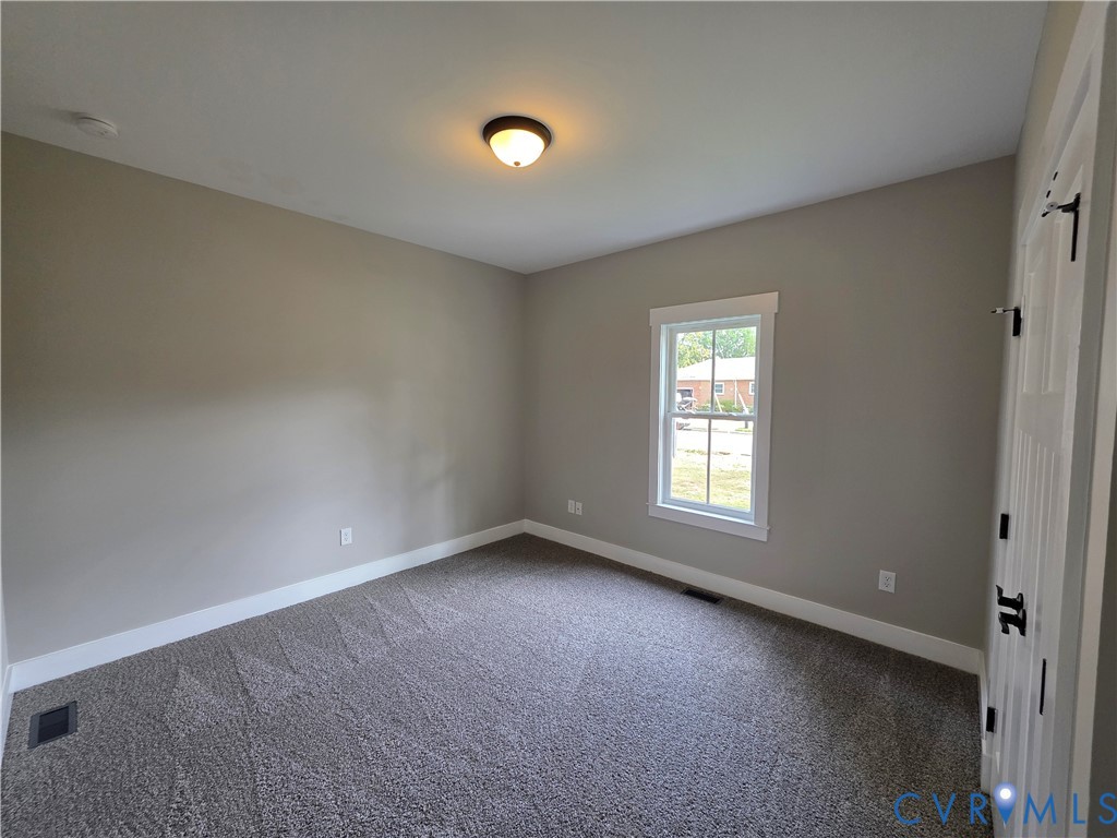 Neutral-toned interior room featuring wall-to-wall carpeting, a multi-pane window with white trim, and a ceiling-mounted flush light fixture