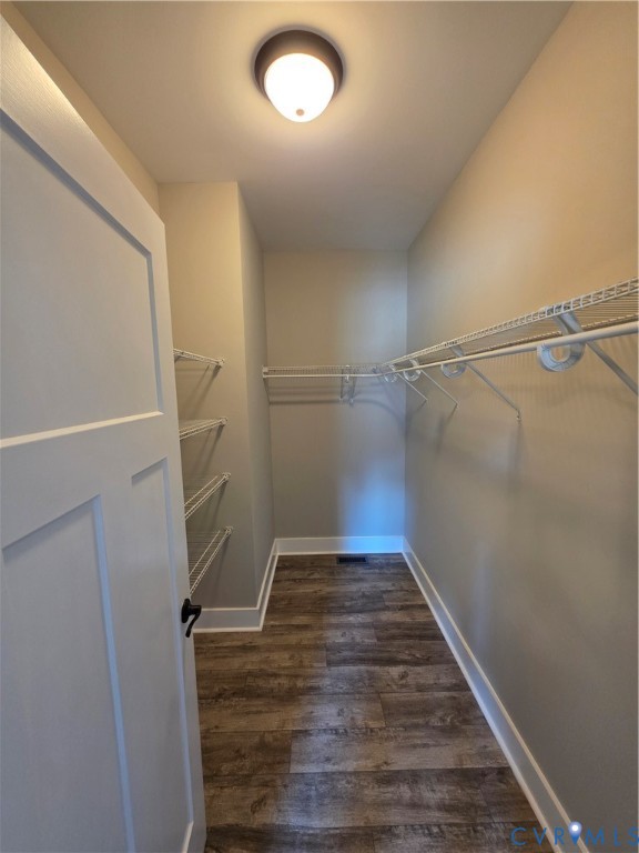 Walk-in storage space featuring wood-finish flooring, white paneled door, flush-mount lighting, and tiered white wire shelving