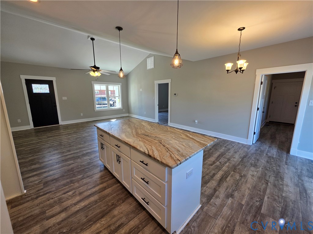 Kitchen island featuring stone countertop, white shaker-style cabinetry, and matte black hardware, complemented by wood-finish flooring and vaulted ceilings