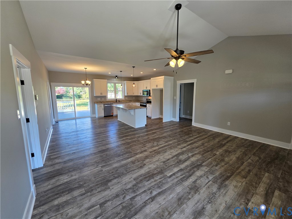 Open-concept interior featuring vaulted ceilings, wood-finish flooring, a kitchen island with stone-surface countertop, white cabinetry, and sliding glass doors