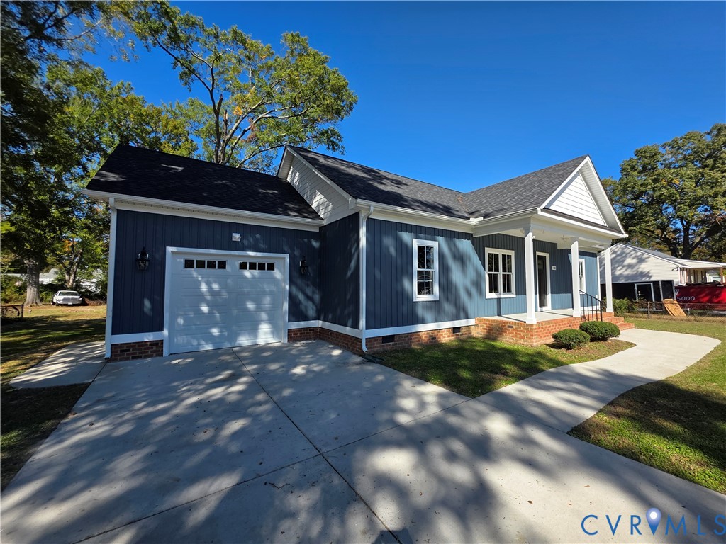Dark-toned vertical siding exterior featuring a covered front porch, brick foundation detailing, multi-paned windows, and an attached garage with a concrete driveway Dark-toned vertical siding exterior featuring a covered front porch, brick foundation detailing, multi-paned windows, and an attached garage with a concrete driveway