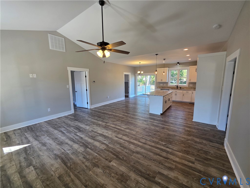 Vaulted ceiling with a central fan, open-concept kitchen featuring an island, and wood-finish flooring throughout