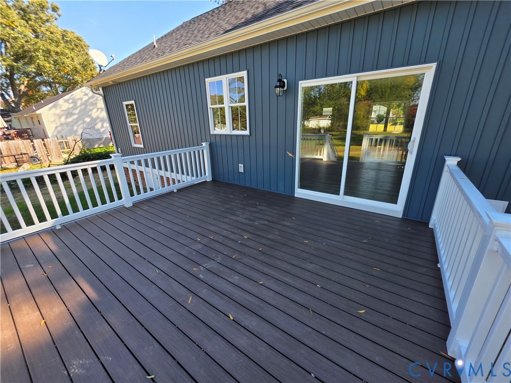 Raised deck featuring dark composite decking, white baluster railings, vertical dark-toned exterior siding, and a sliding glass door Raised deck featuring dark composite decking, white baluster railings, vertical dark-toned exterior siding, and a sliding glass door