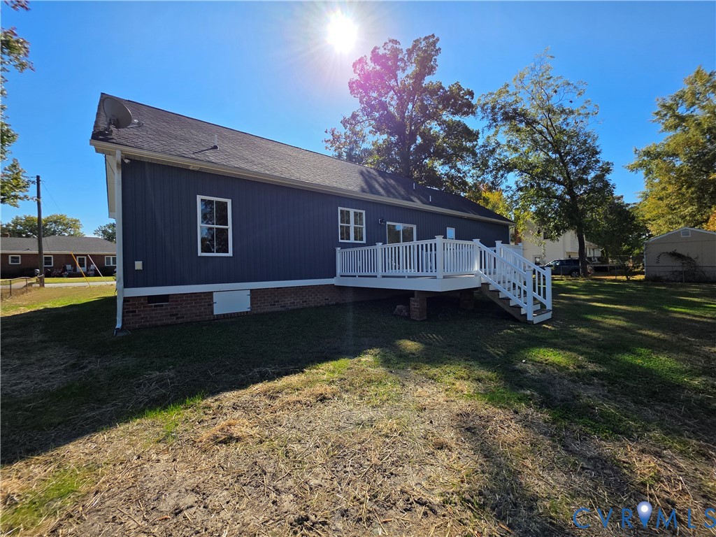 Exterior featuring vertical blue siding, brick masonry foundation, elevated white deck with railing, and mature trees on the grounds Exterior featuring vertical blue siding, brick masonry foundation, elevated white deck with railing, and mature trees on the grounds