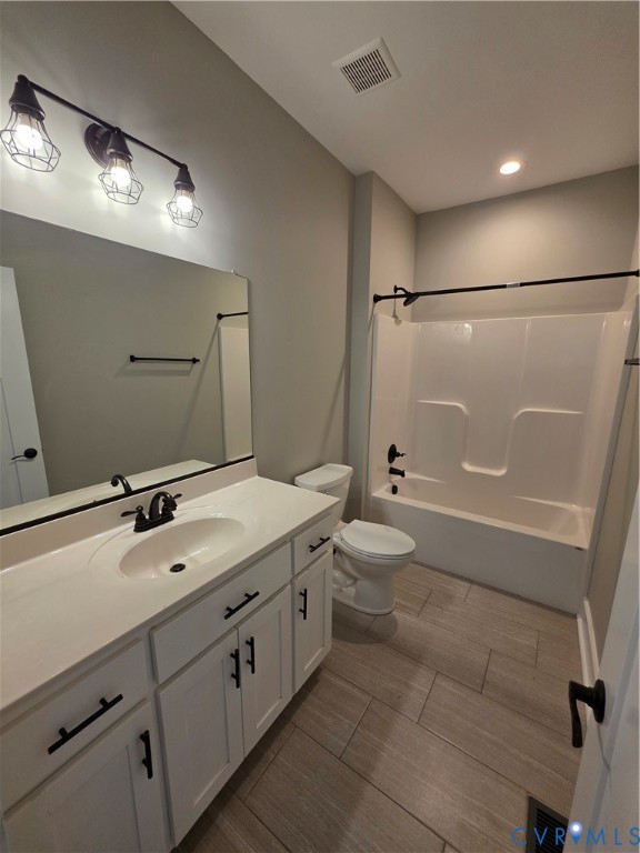 White cabinetry featuring matte black hardware, stone-finish countertop with an integrated oval sink, three-light industrial-style fixture, and wood-finish tile flooring