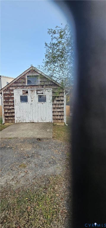 Detached outbuilding featuring shingle siding, a gable roofline, double doors with inset glazing, and a concrete entry pad