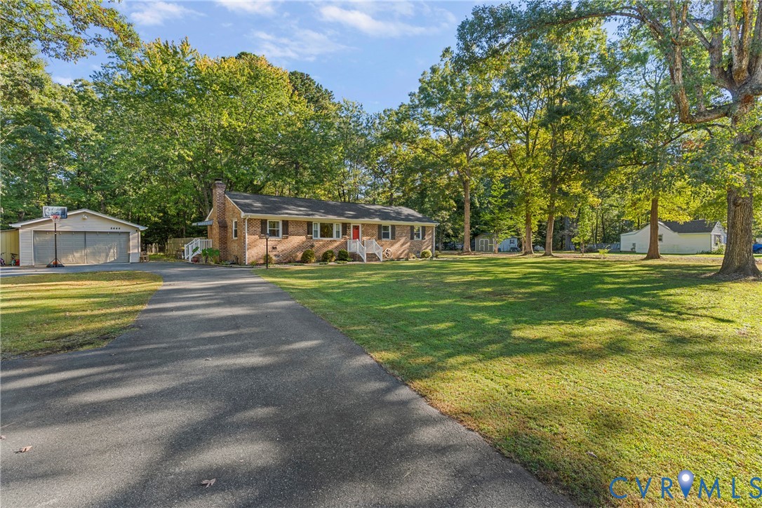 Brick exterior residence featuring a sprawling lawn, paved driveway, detached two-car garage, and mature trees