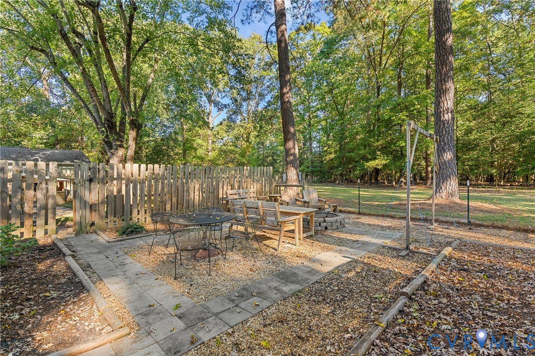 Outdoor living area featuring a paved stone patio, gravel base, stone-encased fire pit, and wood-slat privacy fencing