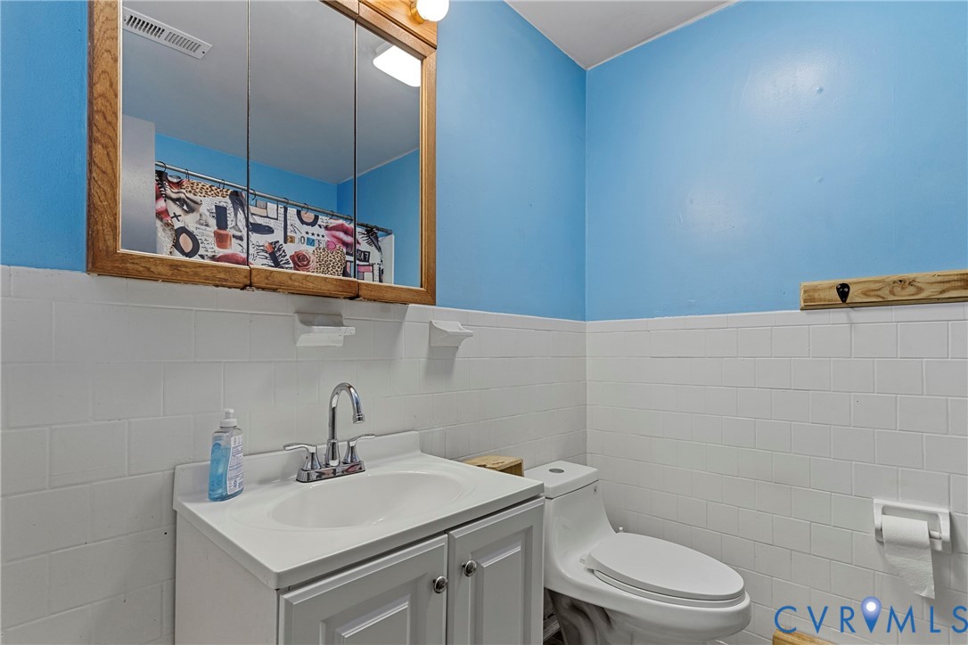 Bathroom featuring white subway tile wainscoting, white vanity with integrated basin and chrome faucet, wood-framed medicine cabinet, and white toilet Bathroom featuring white subway tile wainscoting, white vanity with integrated basin and chrome faucet, wood-framed medicine cabinet, and white toilet