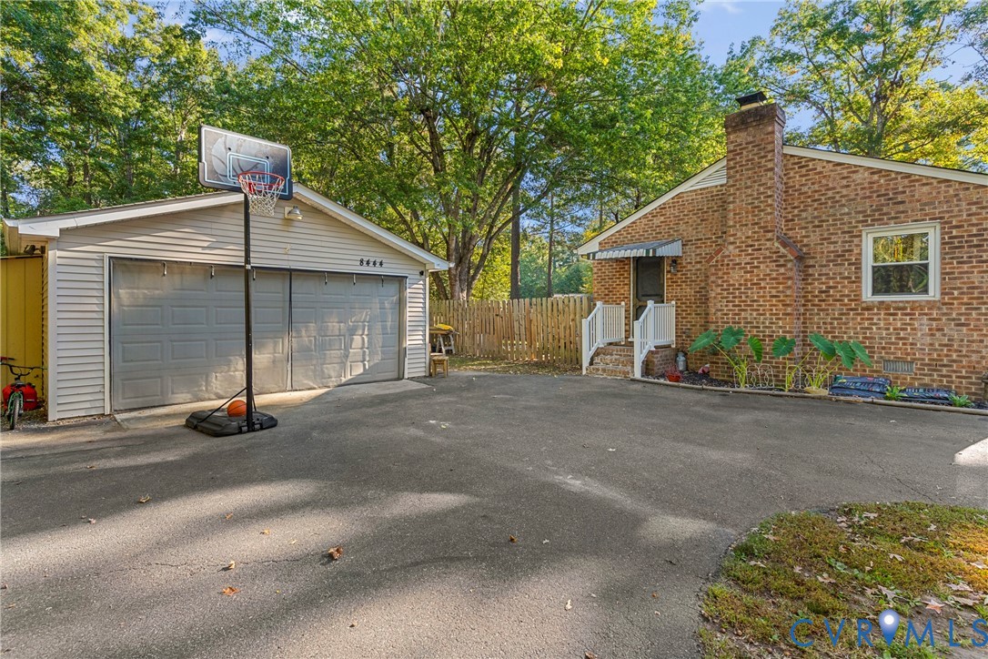 Brick exterior with a prominent chimney, detached garage, asphalt driveway, and wood privacy fencing