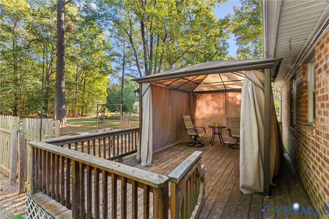 Outdoor wood deck featuring a covered gazebo structure, red brick exterior wall, and perimeter wood fencing