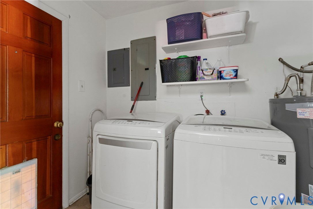 Laundry area featuring washer and dryer hookups, white wall-mounted shelving, solid wood door with brass hardware, and interior electrical service panels