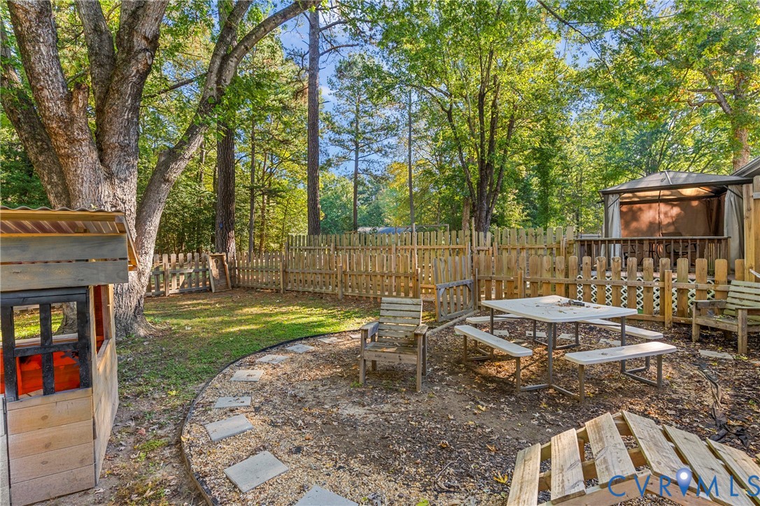 Private backyard featuring a wooden privacy fence, mature trees, an outdoor hardscape area, and a permanent gazebo structure