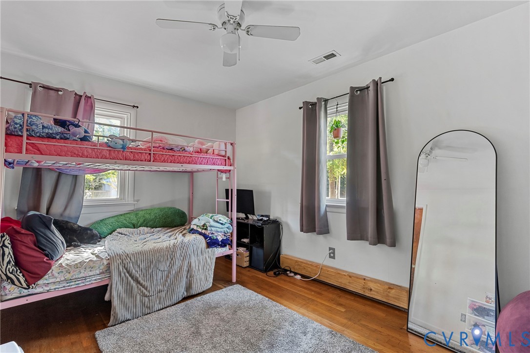 Room featuring wood-finish flooring, dual windows, and a ceiling fan with integrated lighting