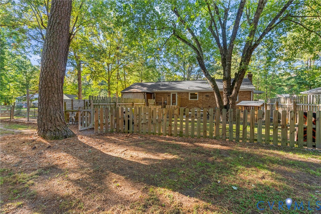 Brick exterior, wooden perimeter fencing, and mature trees on a level lot
