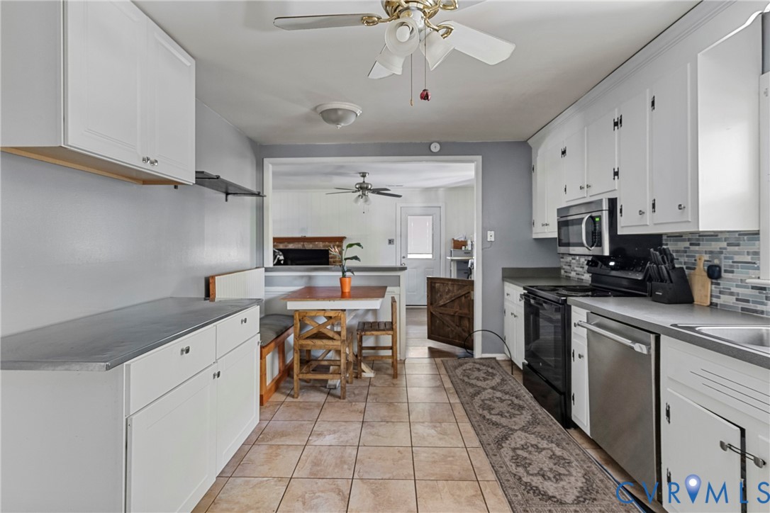 Kitchen featuring white cabinetry, multi-tone tile backsplash, tile flooring, built-in breakfast nook, and stainless steel appliances Kitchen featuring white cabinetry, multi-tone tile backsplash, tile flooring, built-in breakfast nook, and stainless steel appliances