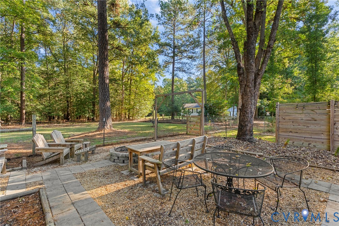 Backyard featuring a paved stone patio, built-in stone fire pit, wood-slat privacy fencing, and mature trees
