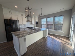 Kitchen featuring white shaker-style cabinetry, an oversized central island with stone-finish countertops, geometric metal pendant lighting, white subway tile backsplash, and wood-finish flooring
