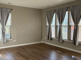 Neutral-toned interior space featuring wood-finish flooring and multiple large windows with installed blinds
