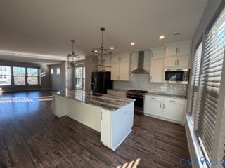 Kitchen featuring white shaker-style cabinetry, a stone-patterned island countertop, stainless steel appliances, a tiled backsplash, and wood-finish flooring