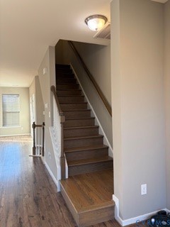 Staircase featuring wood-finish treads, a painted white balustrade with a stained wood handrail, and wood-finish flooring