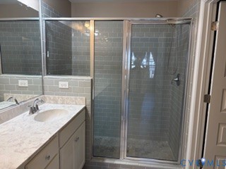 Bathroom featuring a stone-pattern vanity countertop, an undermount sink with a chrome faucet, and a walk-in shower enclosed by a framed glass door with subway-style tile wall surrounds