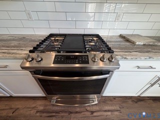 Stainless steel five-burner gas range with central griddle, light-toned stone-patterned countertops, white subway tile backsplash, and shaker-style cabinetry with satin nickel pulls