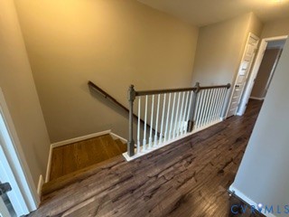 Hallway featuring wood-finish flooring, a wooden handrail, and a white baluster railing