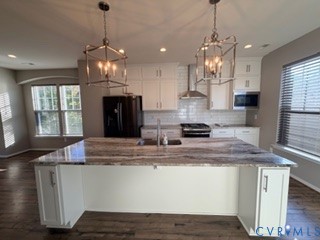 Kitchen featuring a large central island with a stone countertop, white cabinetry, a white subway tile backsplash, stainless steel range hood, and dual lantern-style pendant lights