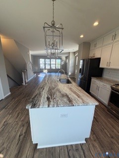 Kitchen featuring a center island with a natural stone countertop, white shaker-style cabinetry, wood-finish flooring, and a suspended lantern-style pendant light