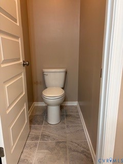 Solid-core panel door featuring satin nickel hardware, tile flooring with stone-finish patterning, and a high-profile toilet