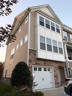 Multi-level exterior featuring light-toned horizontal siding, a multi-paneled stone veneer facade, a multi-pane bay window, and an attached two-car garage with a decorative window pane design