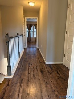 Hallway featuring wood-finish flooring, a white balustrade with dark-finished newel posts, and a dome-style flush mount ceiling light