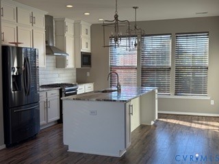 Kitchen featuring wood-finish flooring, white cabinetry, a center island with stone-surface countertop, stainless steel appliances, and dual metal-frame pendant lighting