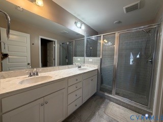 Dual-sink vanity with stone-finish countertop, full-width wall mirror, and walk-in shower with glass enclosure and subway tile surround