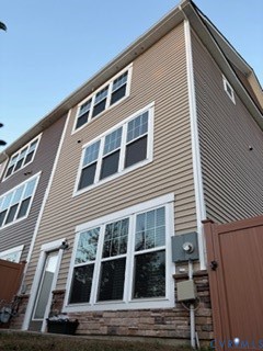 Multi-story exterior featuring tan horizontal siding, stacked stone veneer foundation, white trim detailing, and multiple double-pane windows