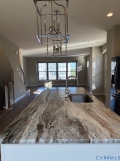 Kitchen island featuring a stone countertop, undermount sink, gooseneck faucet, metal geometric pendant lighting, and white cabinetry