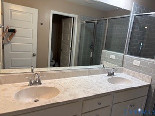Dual-sink vanity featuring stone-finish countertops with integrated basins, chrome fixtures, cabinetry storage, and gray subway tile shower surround