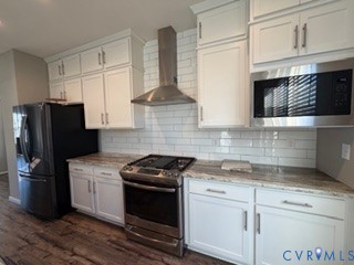 Kitchen featuring white cabinetry, stone-surface countertops, subway tile backsplash, stainless steel appliances, and wood-finish flooring