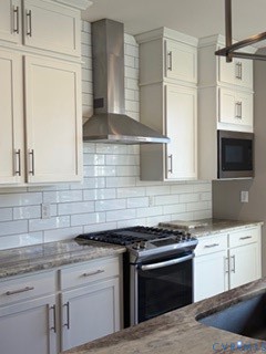 Kitchen featuring white shaker-style cabinetry, stone-patterned countertops, subway tile backsplash, stainless steel range hood, and built-in microwave