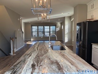 Kitchen island featuring a natural stone countertop, undermount sink with a gooseneck faucet, pendant lighting, wood-finish flooring, and white shaker-style cabinetry